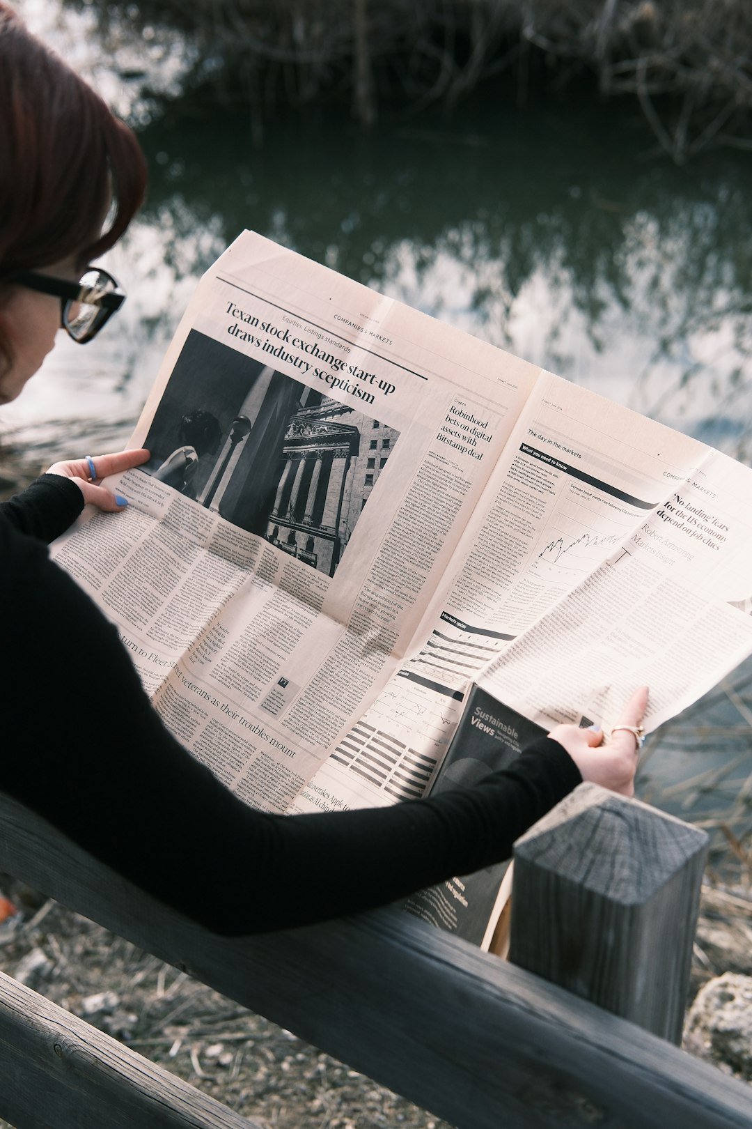 A woman sitting on a bench reading a newspaper