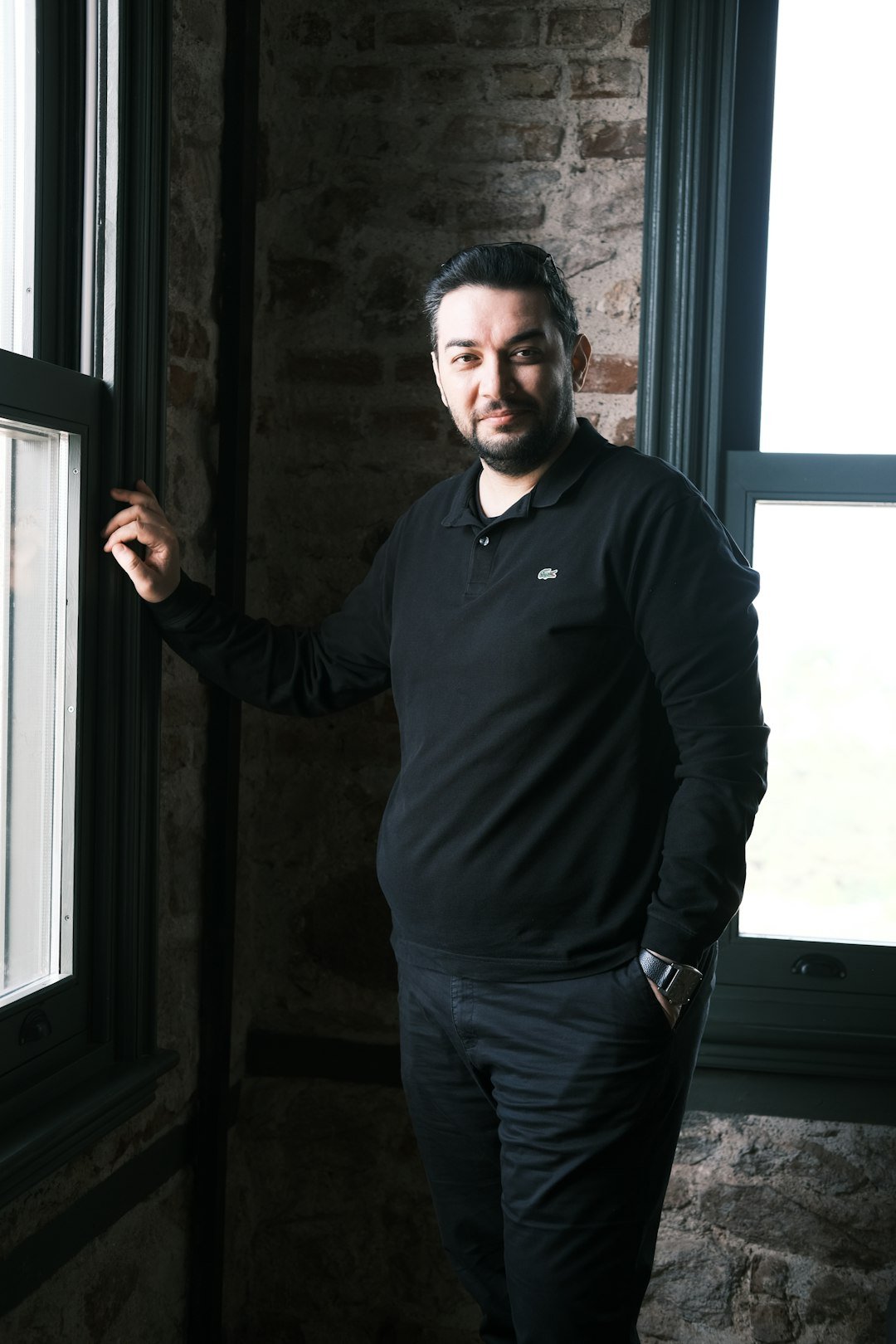a man standing in front of a window next to a brick wall