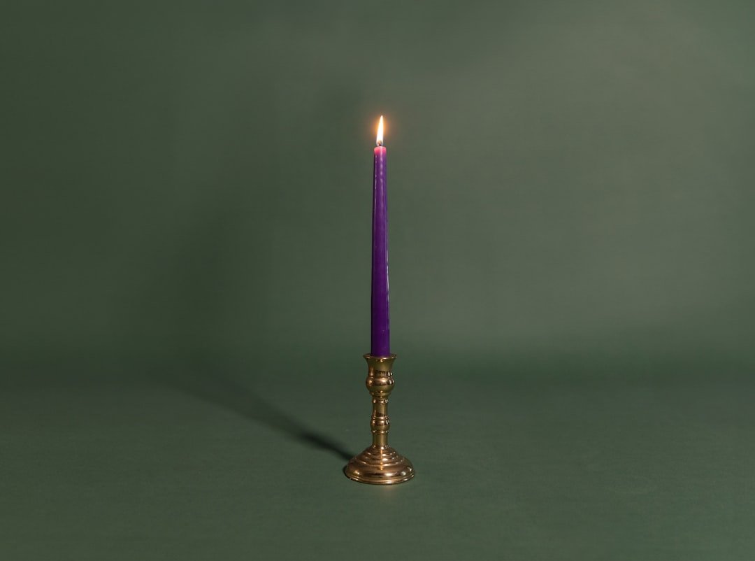 A single purple candle is lit against a green background