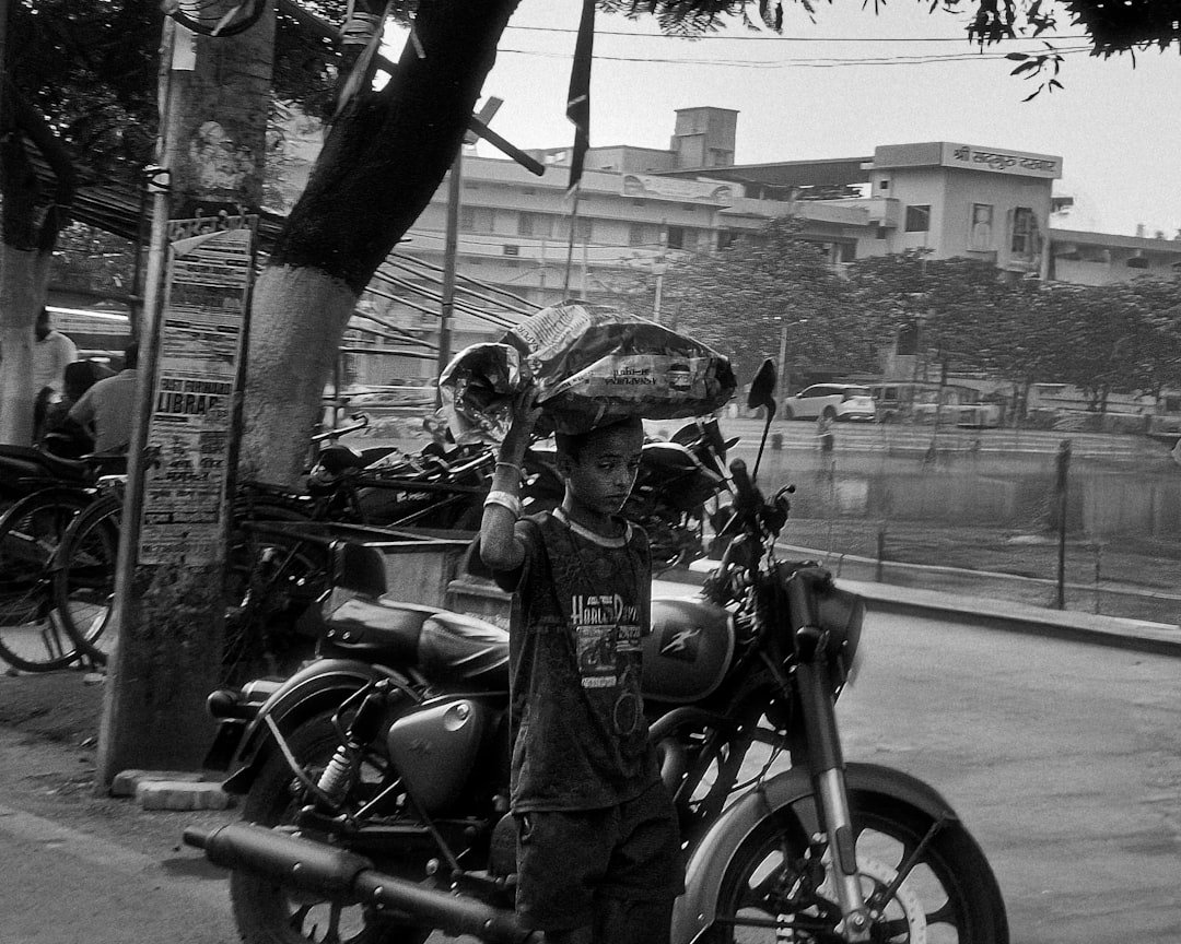 Young boy carries load on head by motorcycle